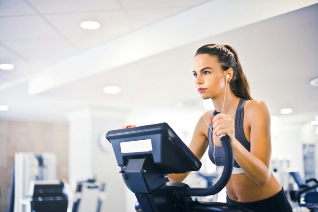 Fit woman in earphones and activewear listening to music and running on treadmill in sports center